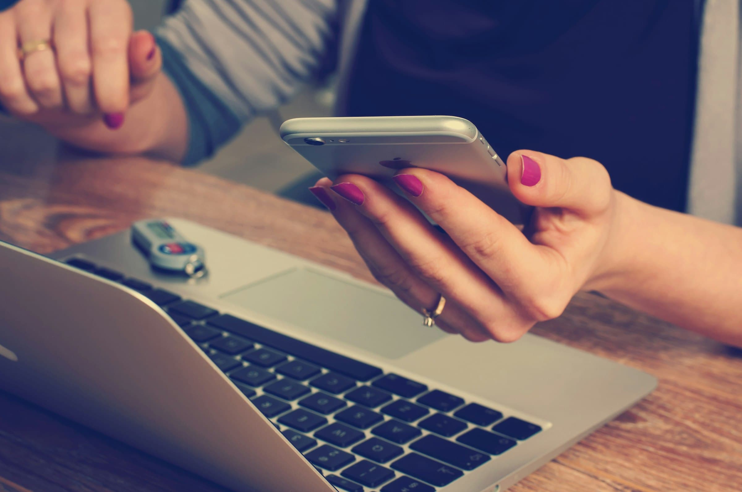 Hand met smartphone boven een laptop op een bureau